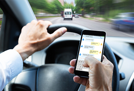 view of driver's hands texting while driving on busy city streets