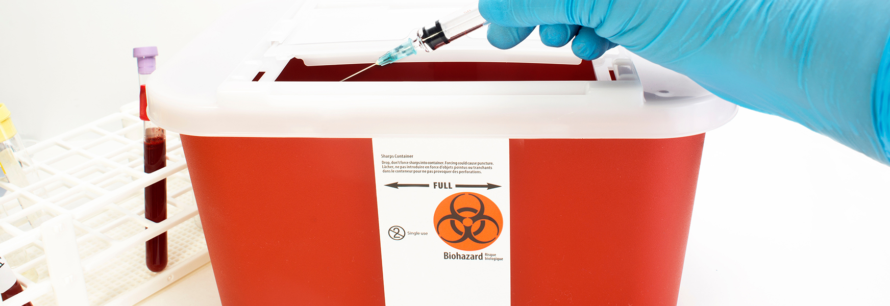 Sharps container with gloved hand depositing needle