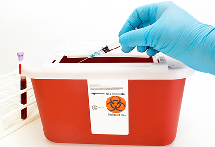 Sharps container with gloved hand depositing needle