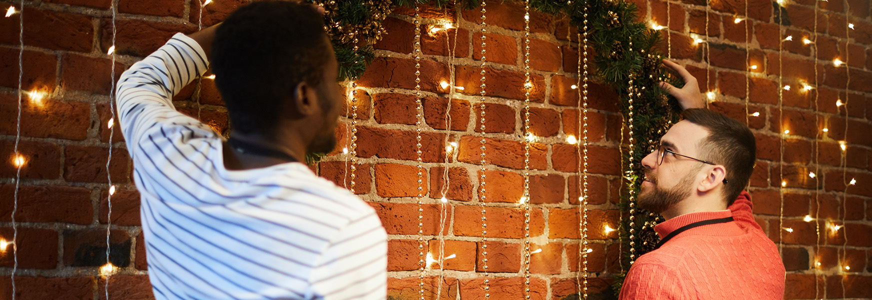 Two office workers hanging large wreath in festive office