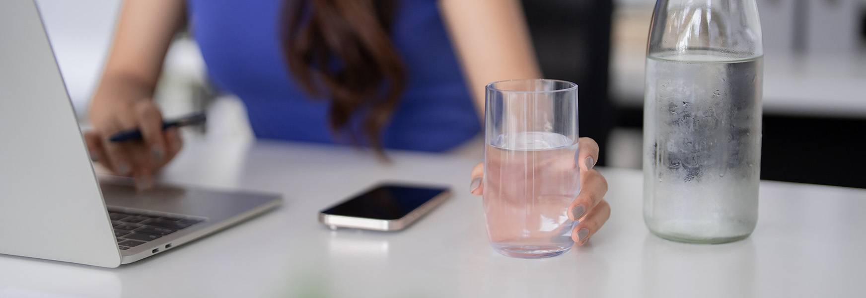 Woman in office reaching for a glass of water