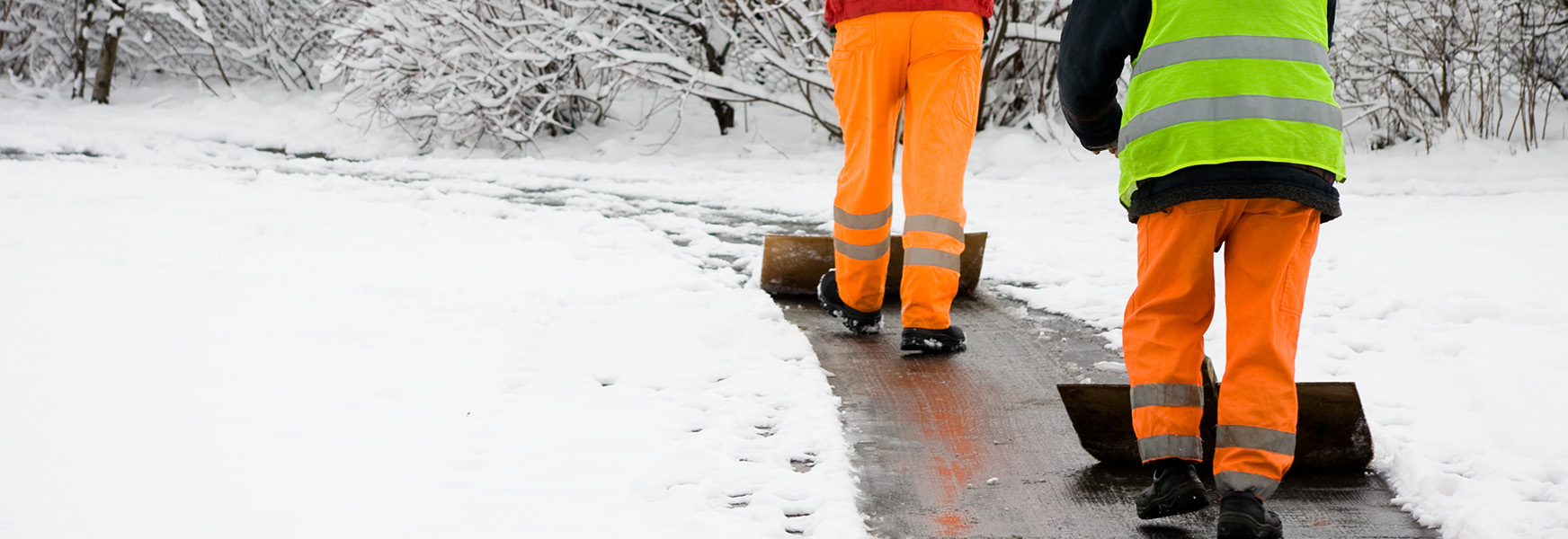 Workers in high visibility gear shoveling snowy walkway