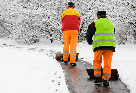 Workers in high visibility gear shoveling snowy walkway