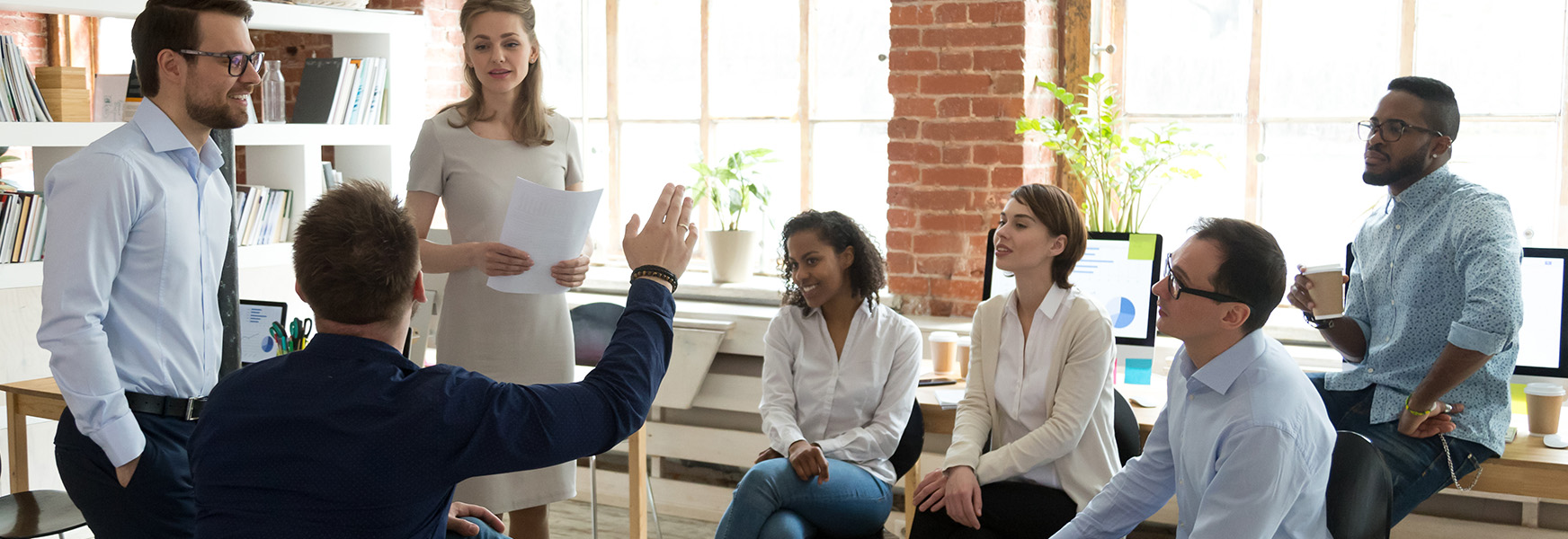 Man raising hand to ask question to diverse workers in office