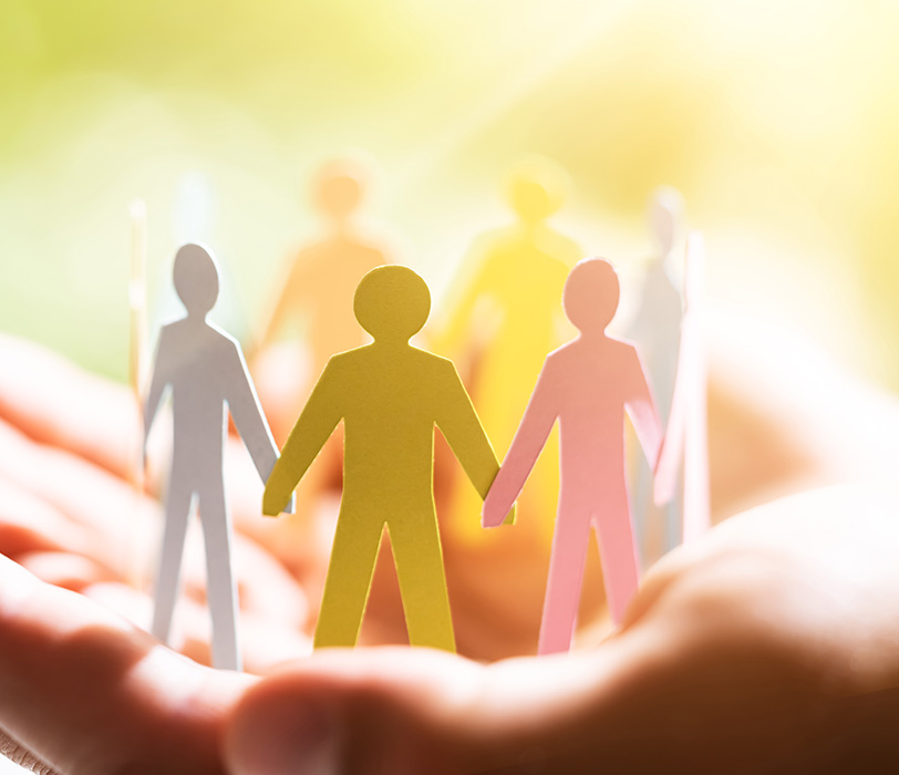 Cupped hands holding paper people joining hands in a circle