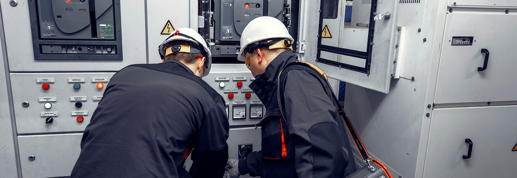 Two technicians wearing PPE inspecting electrical control panel