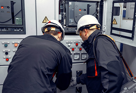 Two technicians wearing PPE inspecting electrical control panel
